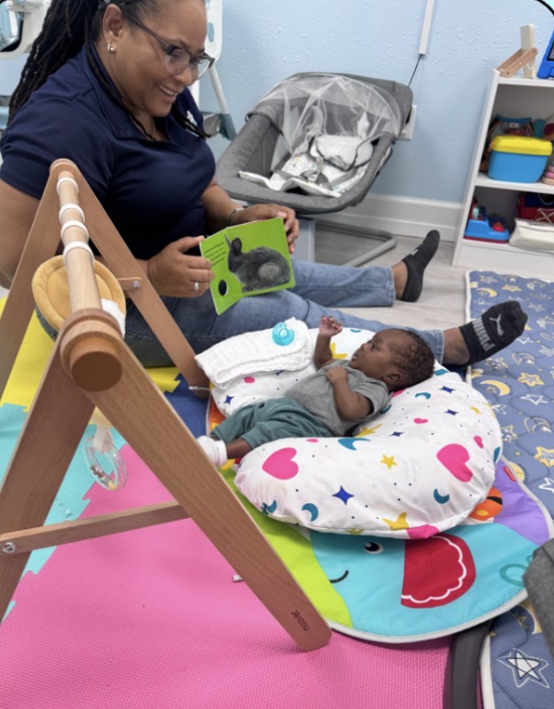 A Dreamland teacher reading a board book with an infant